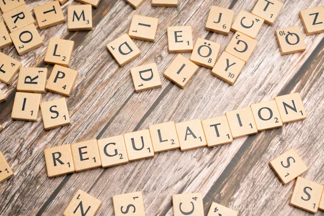 Wooden letter tiles spelling 'Regulation' on a textured wood background, conveying themes of compliance and structure. UK paid social agencies: rules and ethics, gate by gate