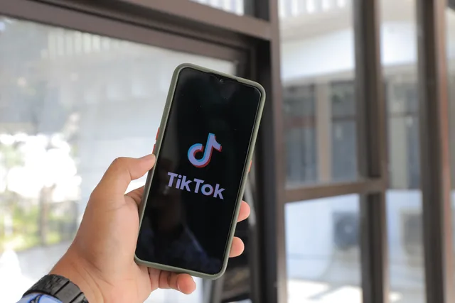 Close-up of a hand holding a smartphone displaying the TikTok app indoors. TikTok advertising agency UK: what to ask before you sign