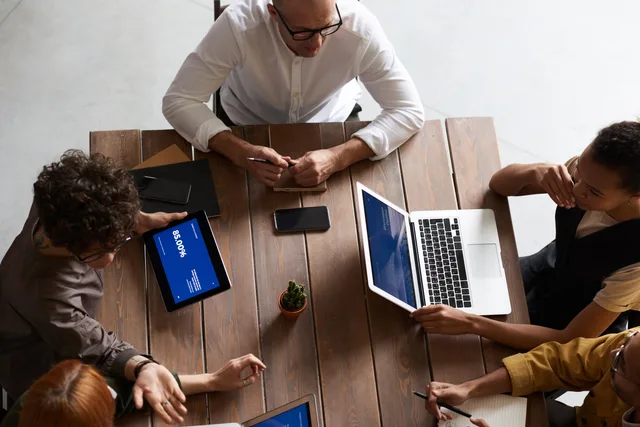 Top view of a diverse team collaborating with laptops and tablets in a modern workspace. White label paid social for UK agencies: a practical guide